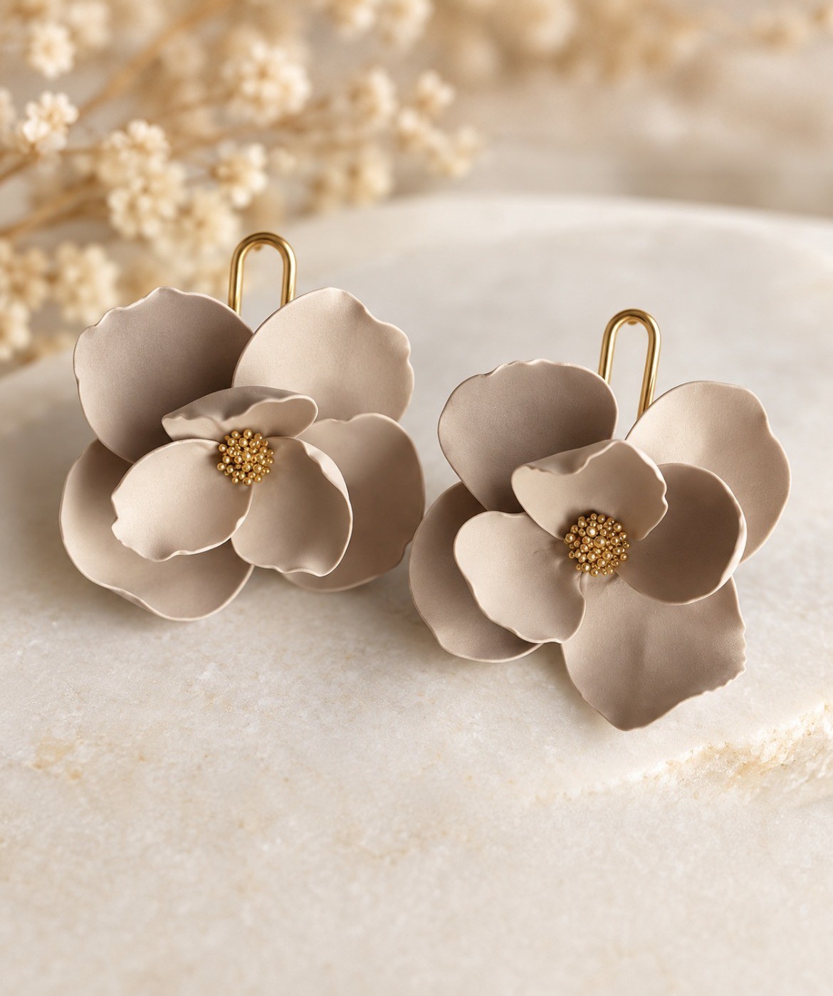 Cream polymer clay flower earrings with gold bead centers on a marble slab